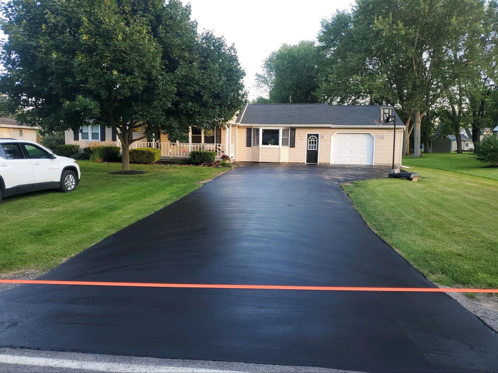 Tan ranch house with a long freshly sealed driveway