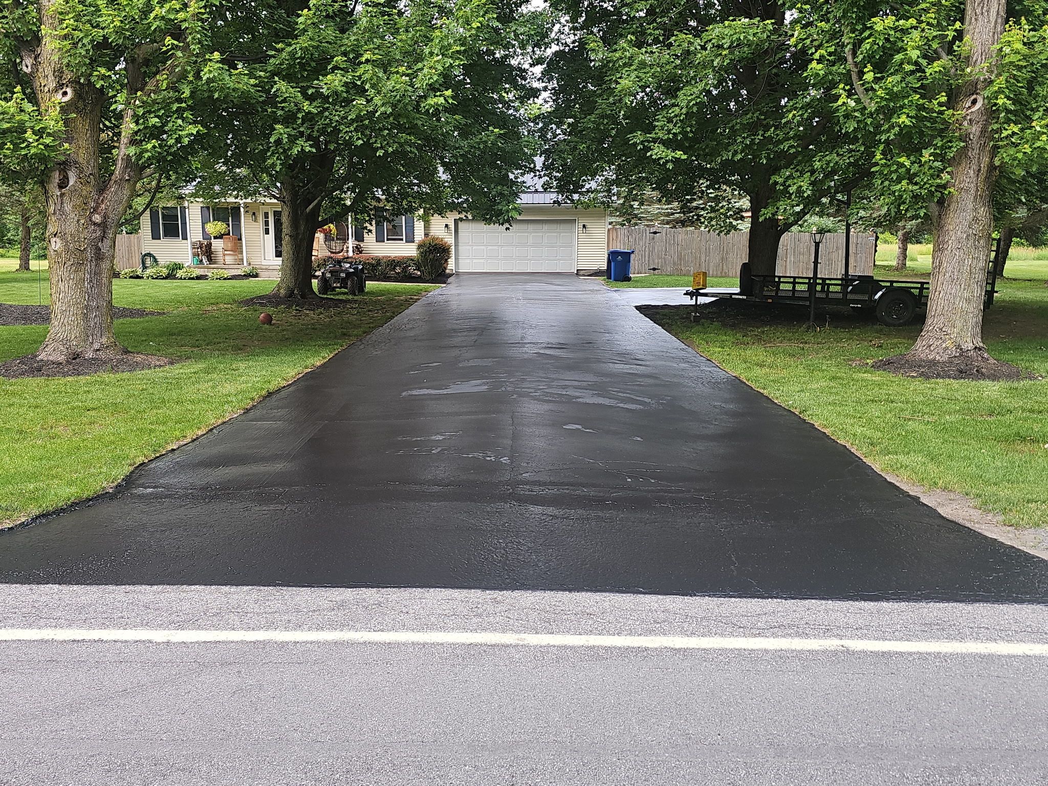 Wide tree-lined residential driveway finished in deep black sealer
